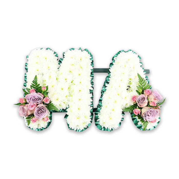 A dignified funeral letter tribute spelling out MA rests against a bright white background, every detail of the floristry clearly visible. Both letters are constructed from a solid bed of fresh white chrysanthemums, their small, daisy-like heads packed so tightly that they form a smooth, almost quilted surface. The petals catch the light in soft highlights and shadows, giving the tribute depth and a feeling of gentle softness, as if the flowers could cradle a final message of love. Encircling each letter, a smart border of deep emerald green, likely satin ribbon or foliage, is carefully pleated or ruffled. This border defines the contours of the M and the A, ensuring their shapes are instantly readable even from a distance at a church or crematorium in Hanwell. At the base of the left leg of the M and the right leg of the A, matching floral arrangements bring in muted colour. These feature a harmonious mix of lilac roses, blush-pink roses, and petite pink spray roses, each flower at a different stage of opening, from tight buds to fully unfurled blooms. Their velvety petals sit among hints of glossy greenery, while a single airy fern frond in each cluster adds a graceful, feathered line that softens the composition. The tribute feels both personal and timeless, perfectly suited to commemorate a beloved mum, mama, or someone known simply by the initials M.A. It is the type of bespoke memorial piece a family in Hanwell might choose to accompany a final journey through local streets filled with familiar memories.
