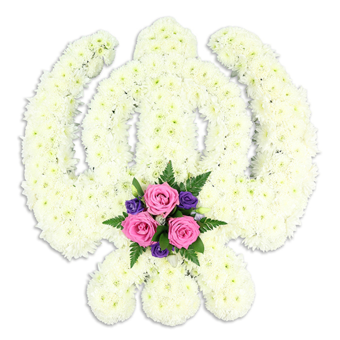 A beautifully composed Sikh Khanda floral tribute dominates the scene, its iconic form created entirely from small white chrysanthemum florets that sit tightly shoulder to shoulder. The florist has sculpted the flowers into the precise outline of the central khanda sword, the surrounding circular chakkar, and the two sweeping kirpans, so that even without colour variation the symbol reads clearly and immediately. The texture is rich and almost quilted, each bloom contributing a soft, feathery petal surface that appears cool and calming against the stark white background. Subtle shadows along the inner curves and edges lend the arrangement depth, as though the Khanda gently lifts away from the backdrop. At the very base, cradled between the lower arms of the kirpans, a contrasting spray of colour offers a tender counterpoint. Three fresh pink roses, their centres tightly coiled yet already opening, are embraced by clusters of deep purple flowers and sprigs of dark green fern. This small posy feels like a whispered message of love and remembrance set within the strength of faith. The tribute could easily be imagined en route from a Hanwell flower shop on Boston Road to a Sikh funeral or memorial near the Brent River Park, delivering both consolation and cultural respect. The luminous white chrysanthemums suggest purity and peace, while the pink and purple accents add emotional warmth, making this design particularly suitable for families who wish to honour a loved one's Sikh heritage through elegantly crafted funeral flowers.