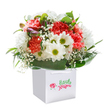 Capturing the joyful spirit found in Hanwell's leafy lanes and riverside walks, this bouquet, set elegantly in a square white gift bag, beams with life and warmth. The lush design is anchored by clusters of peach, coral, and vivid red carnations-their delicate, ruffled petals offering a tapestry of texture and vitality, echoing the colours of a summer sunrise over Brent Valley. Crisp white daisies with bright yellow-green centers perch throughout the bouquet, infusing a playful, uplifting contrast that feels as refreshing as the breeze in Elthorne Park. Wisps of fragrant baby's breath, sprinkled with care, add a soft innocence and airy dimension, reminiscent of gentle clouds drifting across Hanwell's skies. Peeking shyly from the left, a handful of purple-tinged buds promise new blooms to come, adding depth and curiosity to the mix. Enveloped by a lush border of glossy, deep green leaves, the arrangement is rounded and complete, its fullness speaking to careful hands and a nurturing spirit. The gift bag, fitted with broad ribbon handles, is ideal for those times you wish to offer a gesture of celebration or comfort-be it a birthday surprise or a cheerful delivery to a loved one's door in Hanwell. Against a brilliantly white background, every petal and leaf shines in crisp focus, emphasising the bouquet's unfailing freshness and local artistry. This radiant display embodies the care and pride of Hanwell's florists, delivering happiness and heartfelt wishes throughout the community.