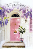 In this scene, a charming entranceway is transformed into a gentle celebration of a new chapter, much like the feeling of unlocking a first home near Hanwell's tranquil green spaces. A pale pink front door stands in the centre, painted in a muted, almost chalky blush that glows softly where the light touches it. The surrounding walls are whitewashed, their slightly textured surface giving the impression of age and character rather than stark newness. To one side, a single light-toned shutter balances the composition, helping guide the eye towards the flowers and the door itself. Overhead, wisteria drapes in abundant cascades, its dangling clusters of lavender and lilac flowers forming an arch that feels both protective and celebratory. The blooms hang in layered strands, each one laden with delicate petals that suggest a light, powdery fragrance, the sort you might catch while strolling through Brent Lodge Park when the season is at its sweetest. At the threshold, resting just before the door, a simple grey florist's bucket cradles a full arrangement of creamy white roses. These roses are open and rounded, their petals curling outward in soft spirals, some with gentle ivory centres that deepen their dimension. Tufts of fresh, green foliage nestle in between, adding small bursts of colour and giving the bouquet a natural, hand-gathered look rather than anything too formal. A soft pink ribbon wraps around the lower part of the bucket, tied neatly into a bow that echoes the warmth of the door and gently anchors the display. Light drifts through the wisteria, casting fine, lacy shadows across the step and doorframe. The overall mood is tender and hopeful, like a quiet housewarming gift delivered by a caring Hanwell florist, marking the beginning of life in a new home with flowers that speak softly of welcome, comfort, and the promise of many happy returns through that doorway.